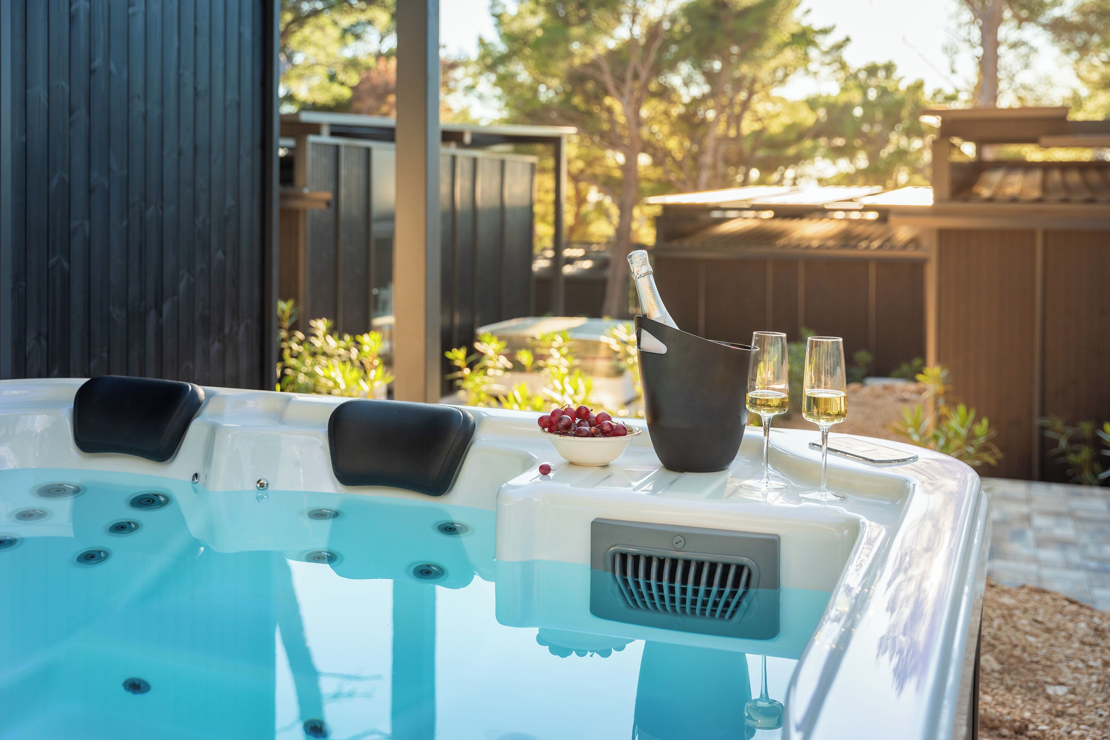 A hot tub with two black lounge chairs, a bowl of grapes, and two glasses of champagne.