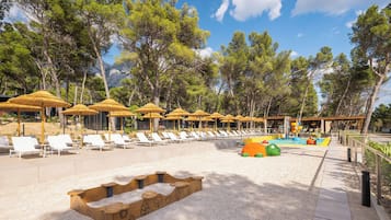 Ein Strandresort mit Liegestühlen, Sonnenschirmen und einem Spielbereich für Kinder.