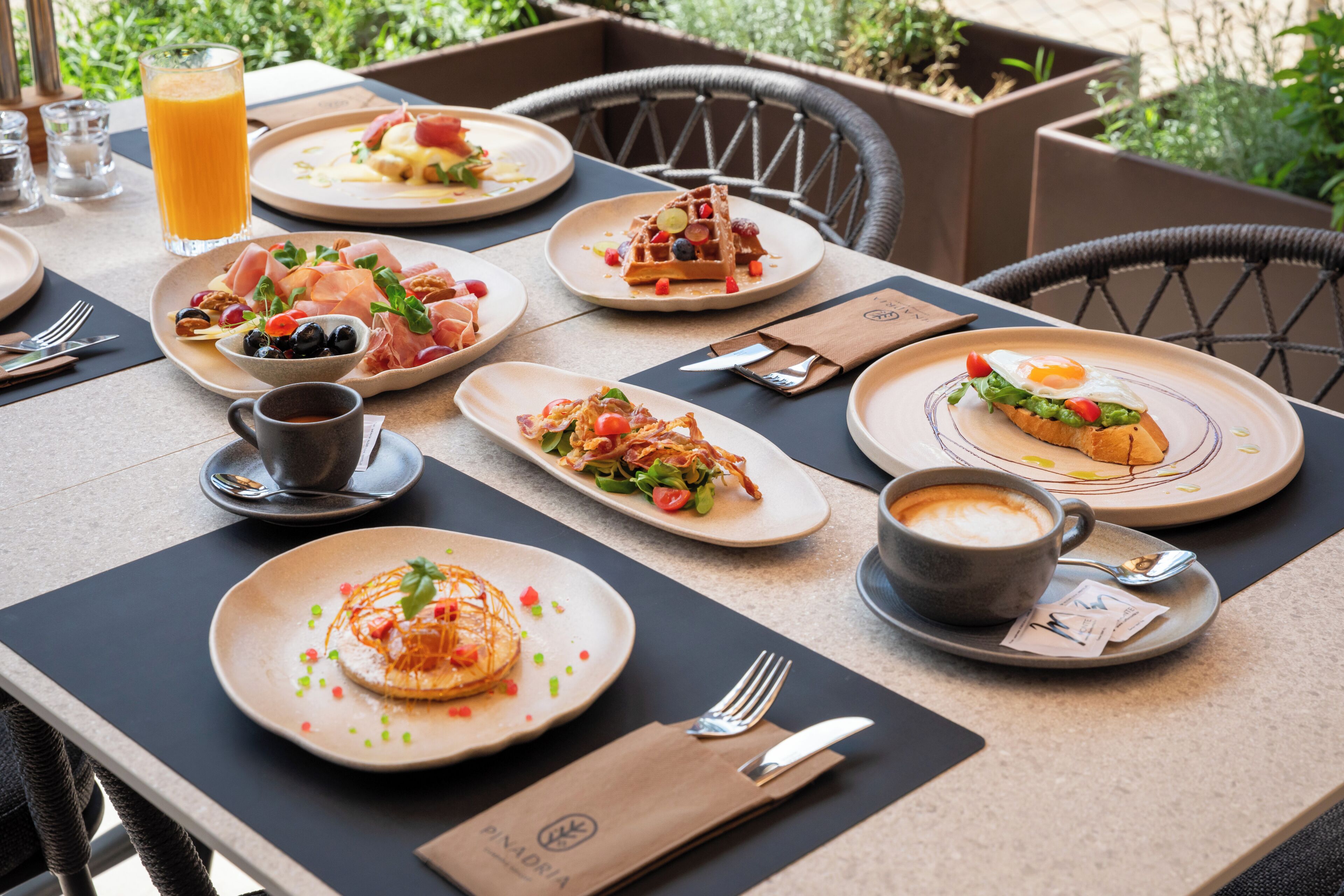 A table set with various breakfast dishes, a glass of orange juice, and a cup of coffee.