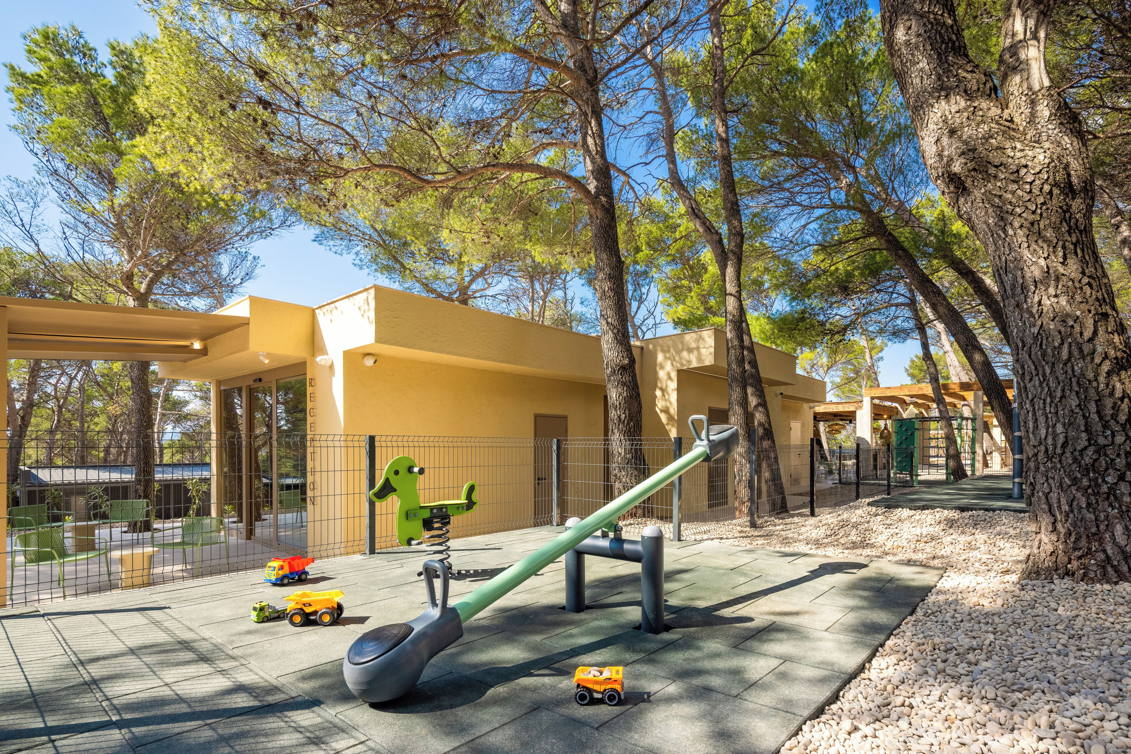 Un parque infantil con sube y bajas, un dinosaurio de juguete verde y camiones de juguete.