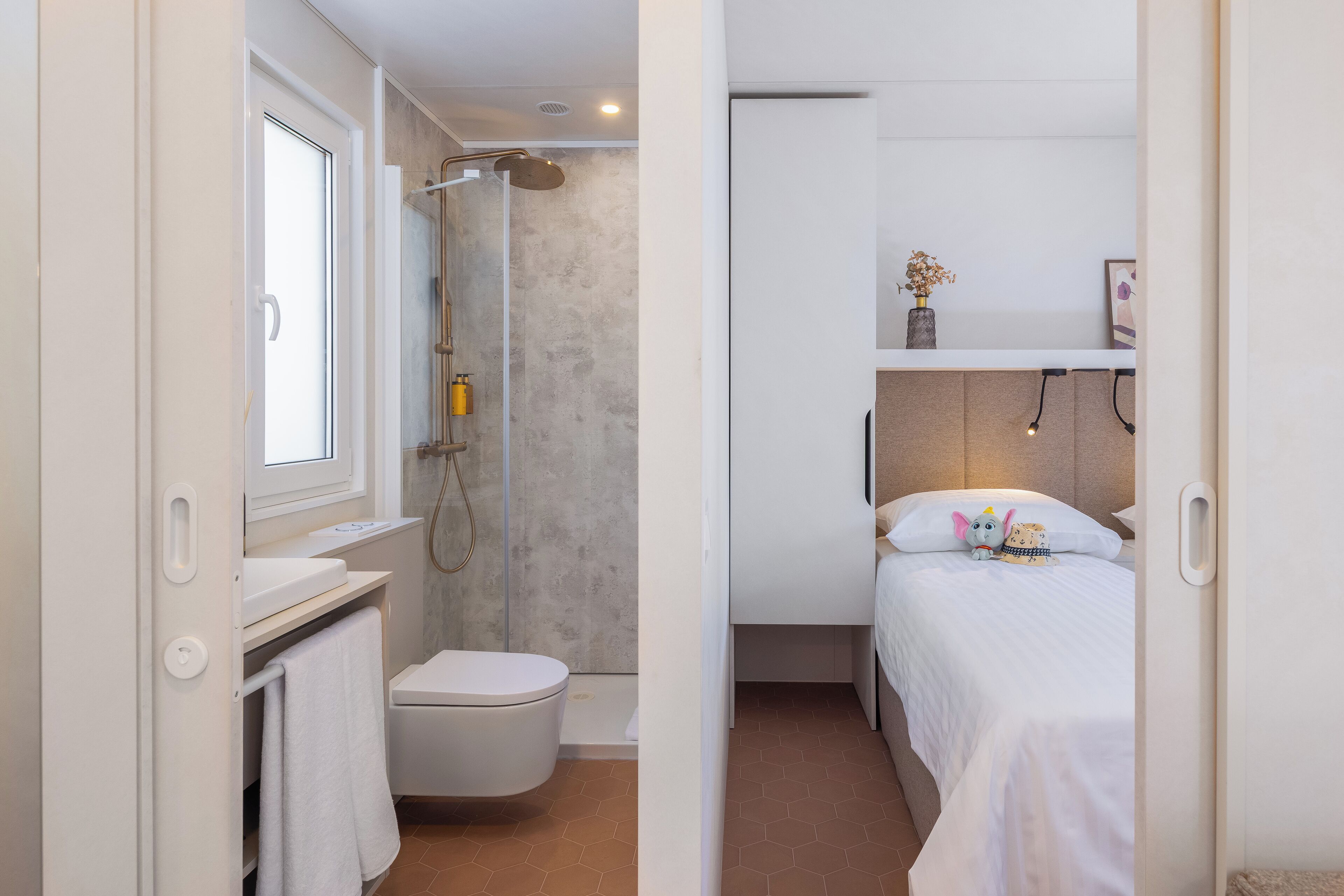 A compact bedroom with a single bed, a bedside table, and a small shelf with a vase.
