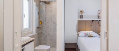 Un dormitorio compacto con una cama individual, una mesita de noche y un estante pequeño con un florero.