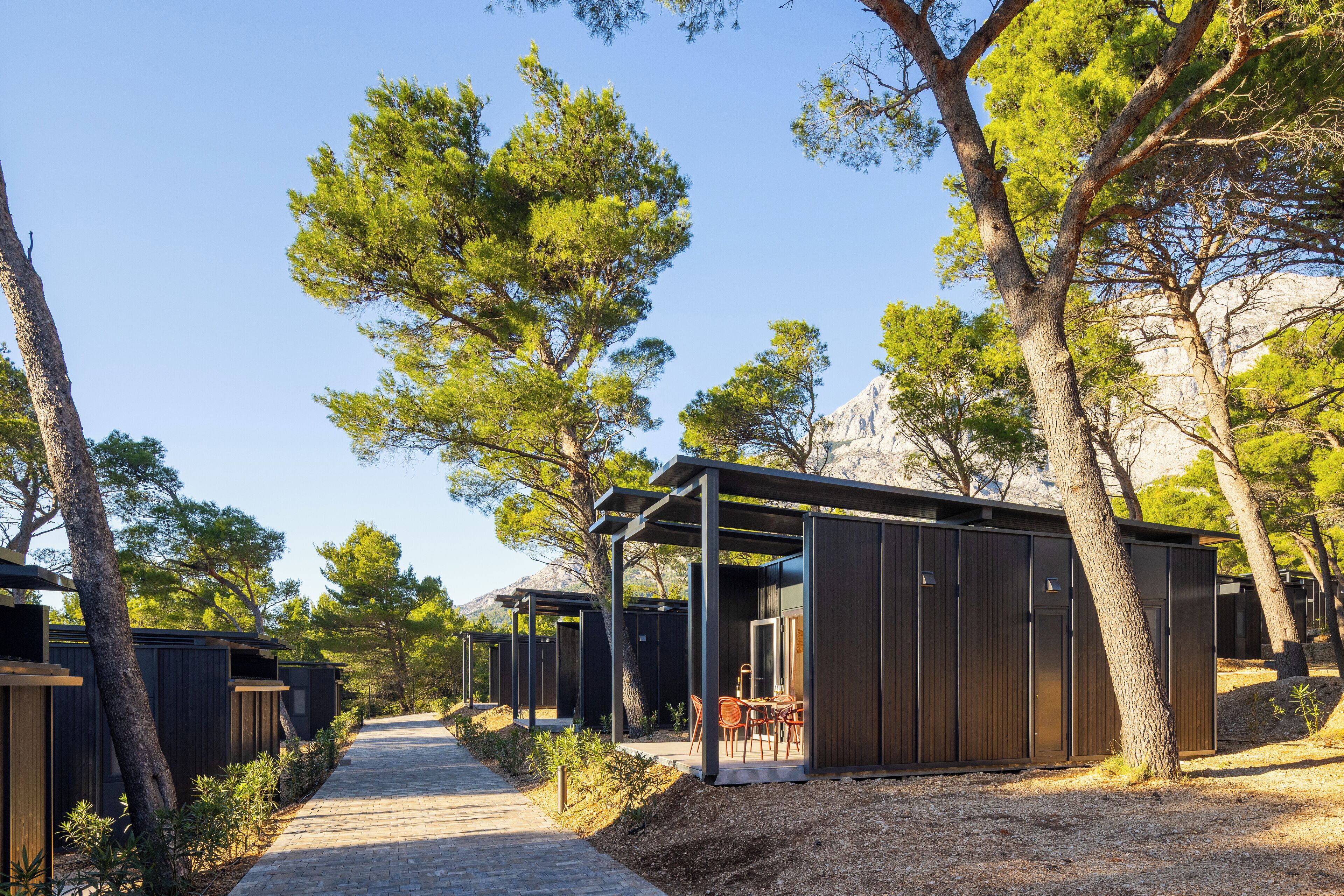 File di cabine con posti a sedere esterni, immerse tra alberi e sotto un cielo sereno.