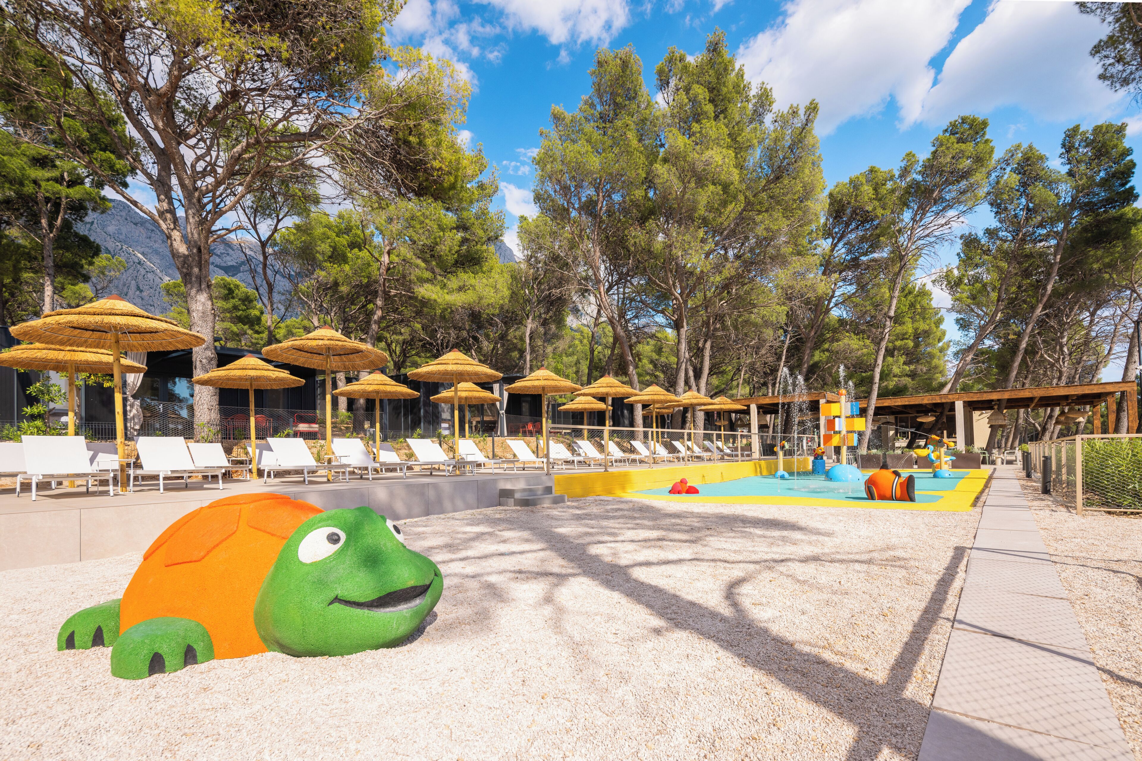 A beach area with lounge chairs, umbrellas, a pool, and a large turtle sculpture.