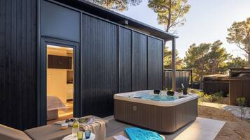 Un área moderna de hidromasaje al aire libre con una terraza de madera, sillones de descanso y una pequeña mesa con bebidas.