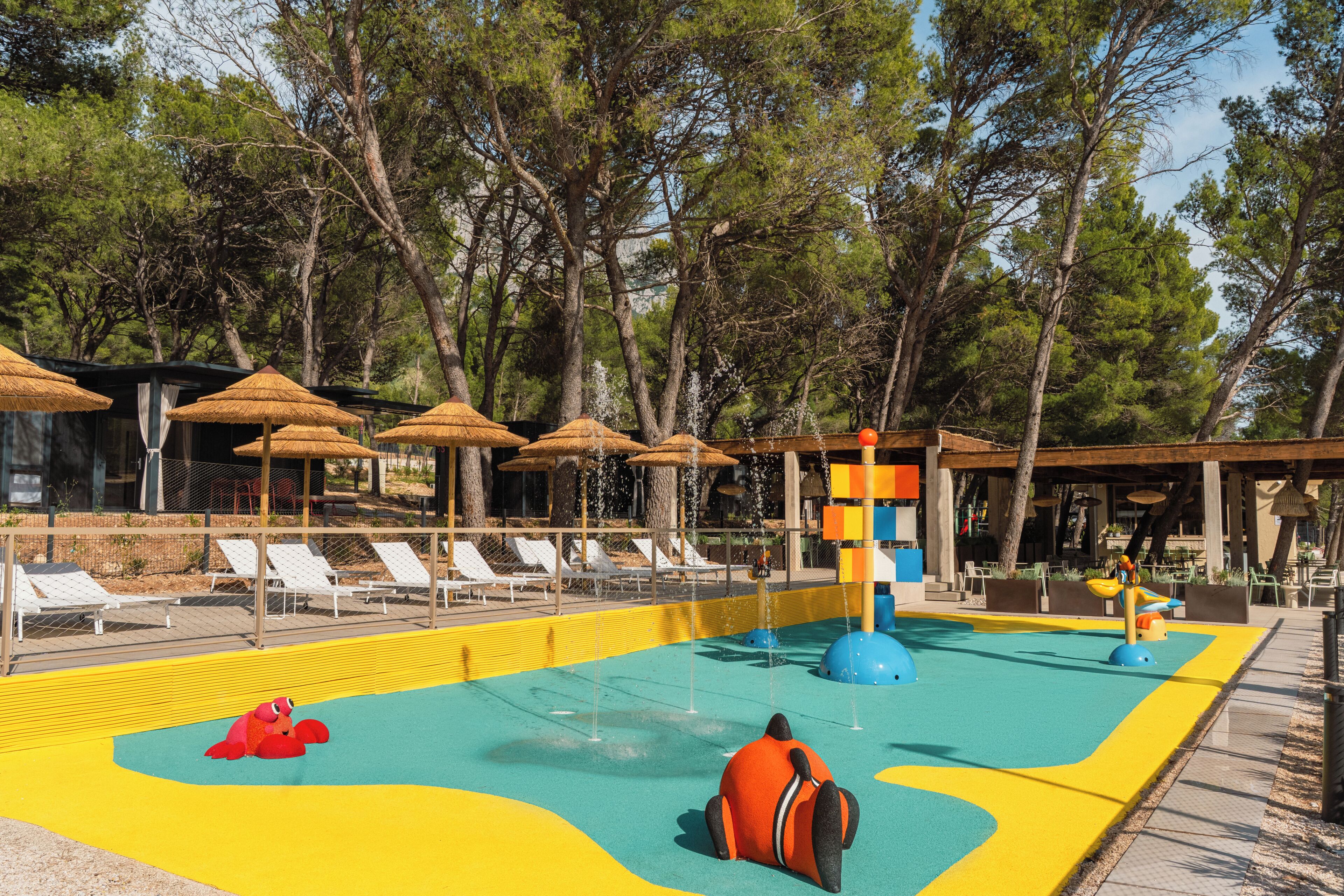 Area piscina con lettini, ombrelloni e area giochi d'acqua.