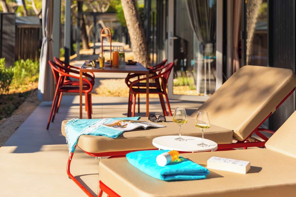 A sunlit outdoor seating area with lounge chairs, a table with drinks, and a view of the garden.