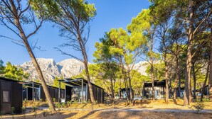 A row of modern cabins with large windows, surrounded by trees and mountains in the background. - Pinadria Camping Resort (Baška Voda)