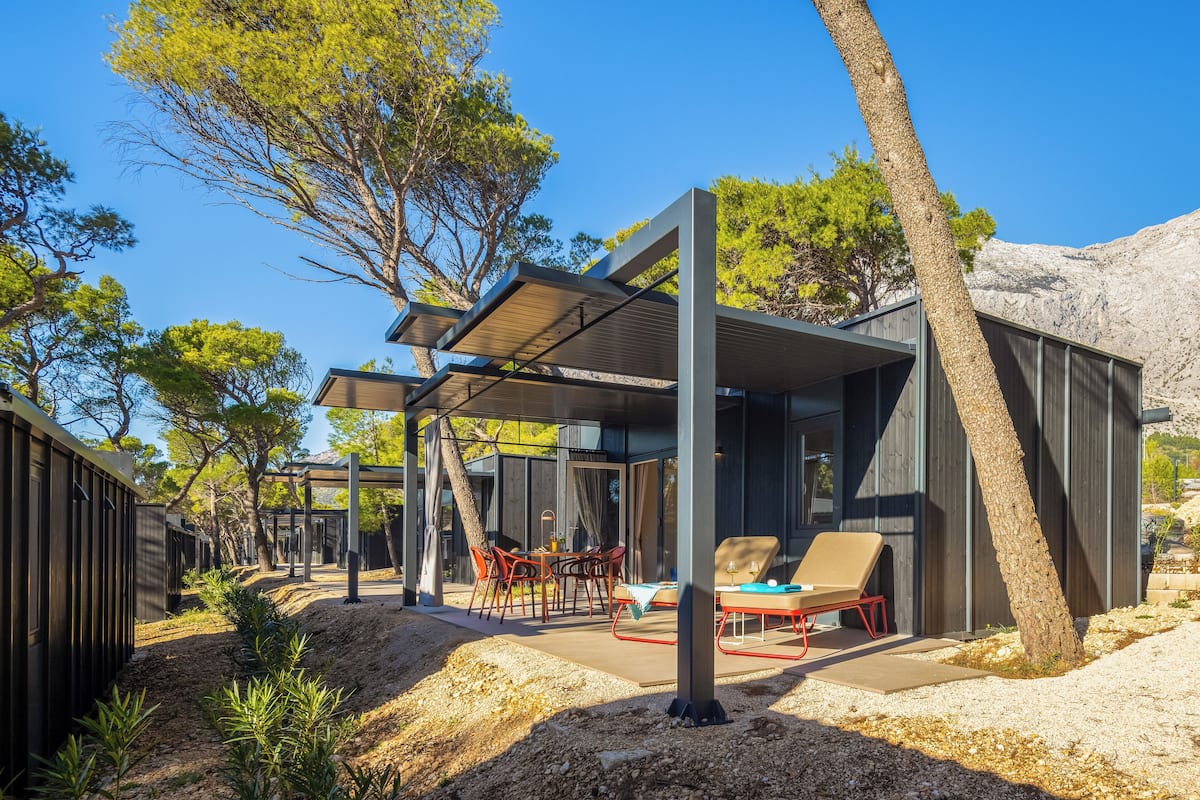 A modern outdoor seating area with a table and chairs, surrounded by trees and a mountainous backdrop.