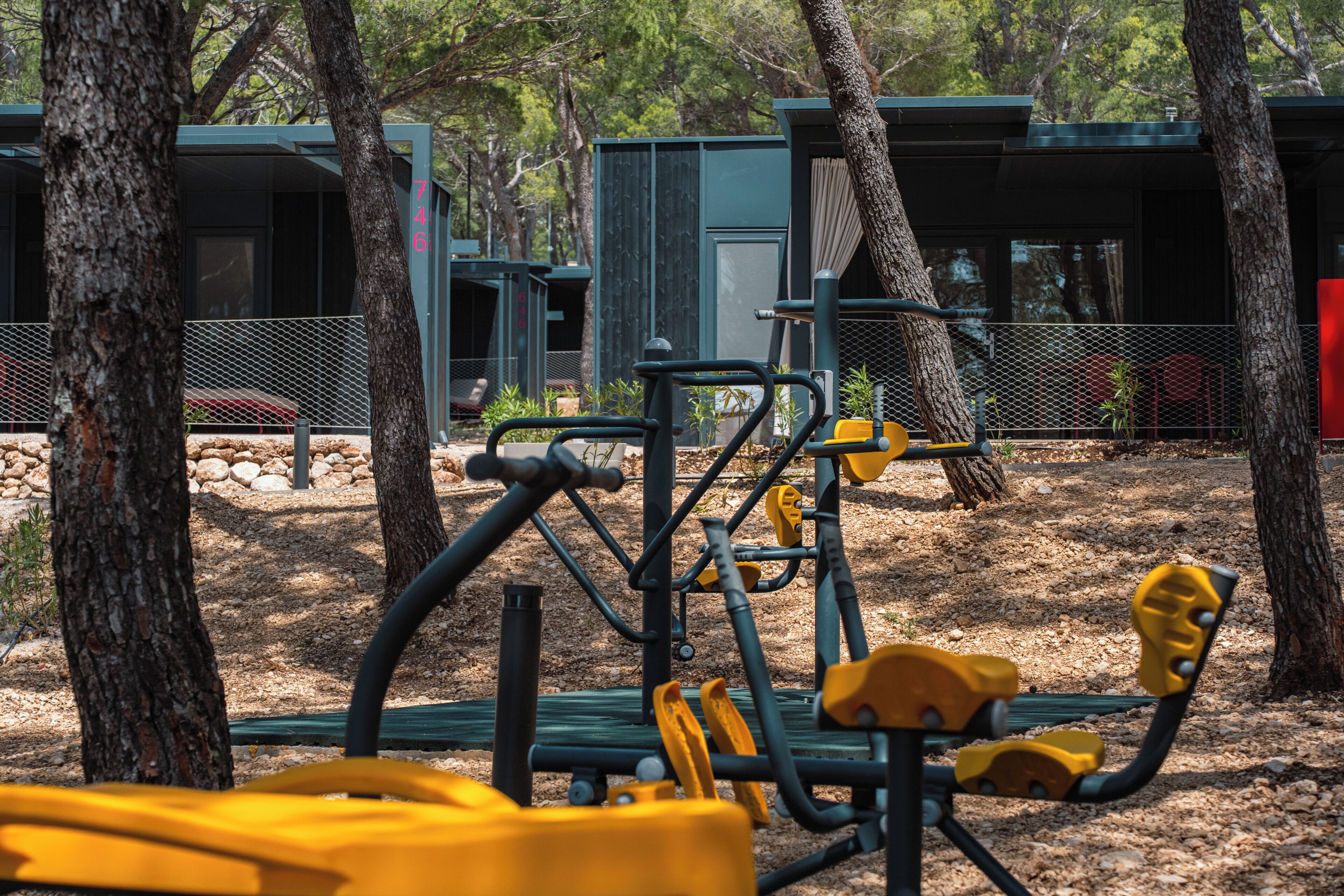 Outdoor exercise equipment, trees, and a building with a metal fence.