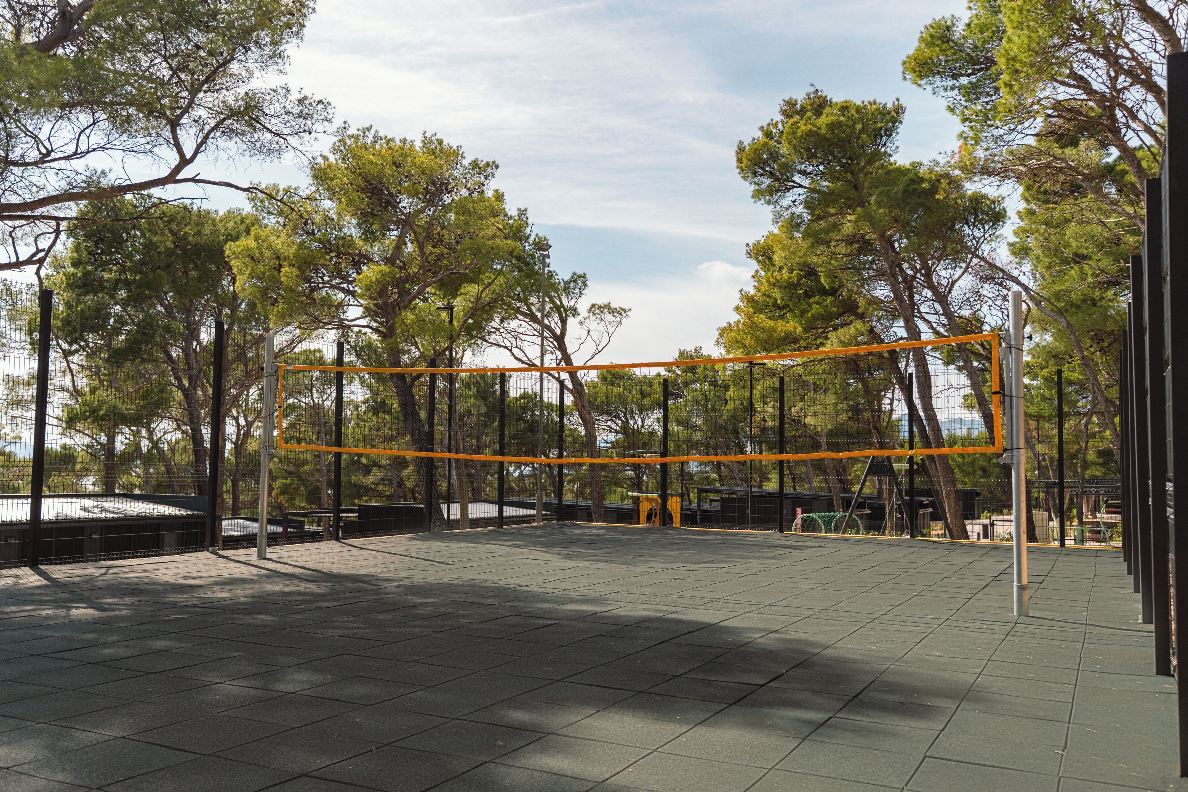 An outdoor sports court with a net, surrounded by trees and a fence.