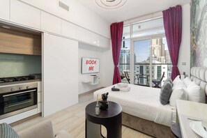 Ett modernt hotellrum med ett litet pentry, en säng med utsikt över staden och ett litet runt bord.