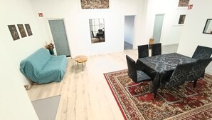 Een moderne kamer met een blauwe kruisje, een klein rond tafeltje, en een eethoek met een tafelkleed met patroon en zwarte stoelen.