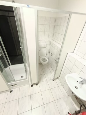 A bathroom with a toilet, a sink, and a shower area. - Lumara Apartment for 10 (Aschaffenburg)