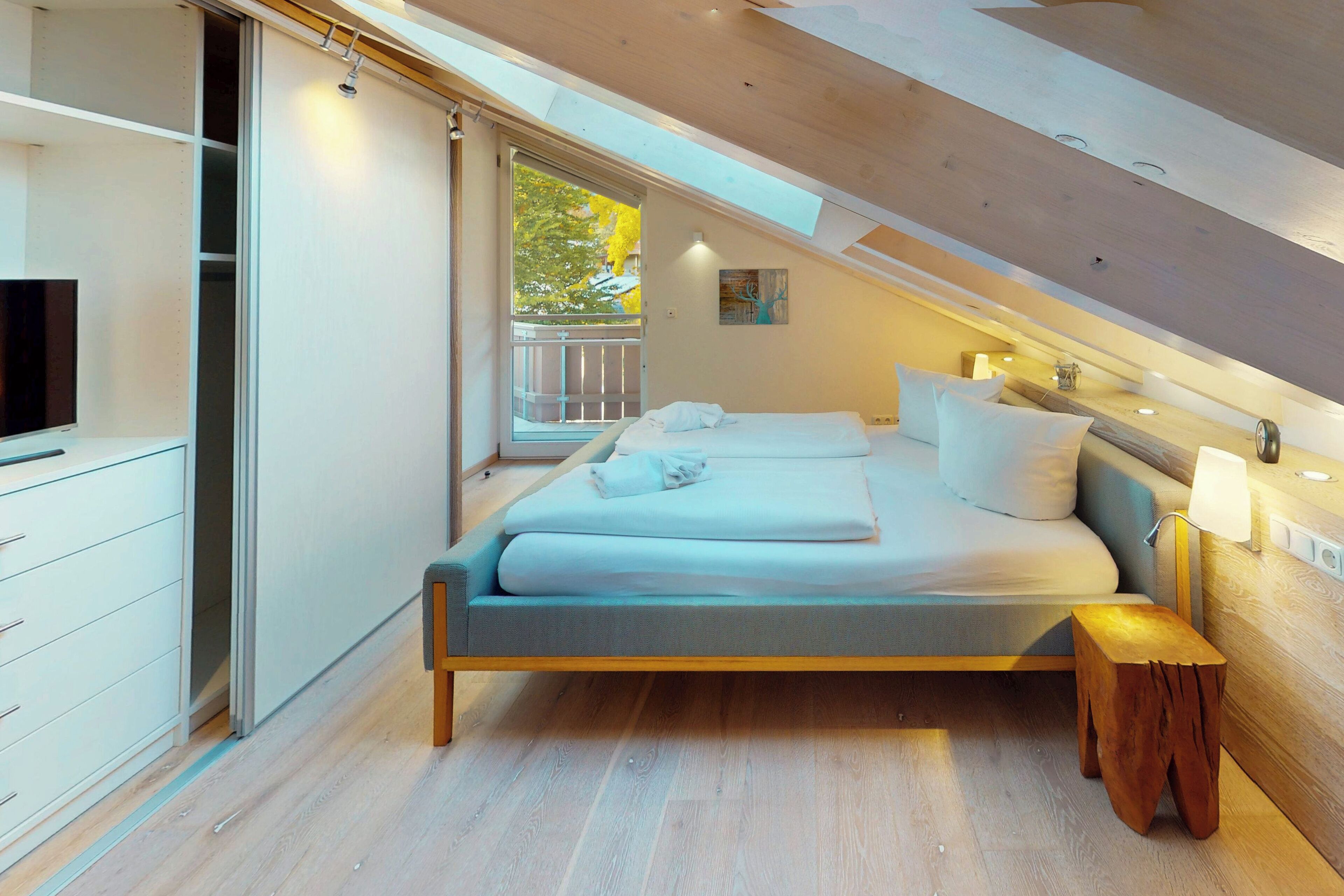 A modern bedroom with a skylight, a bed with pillows, a bedside table, and a TV on a stand.