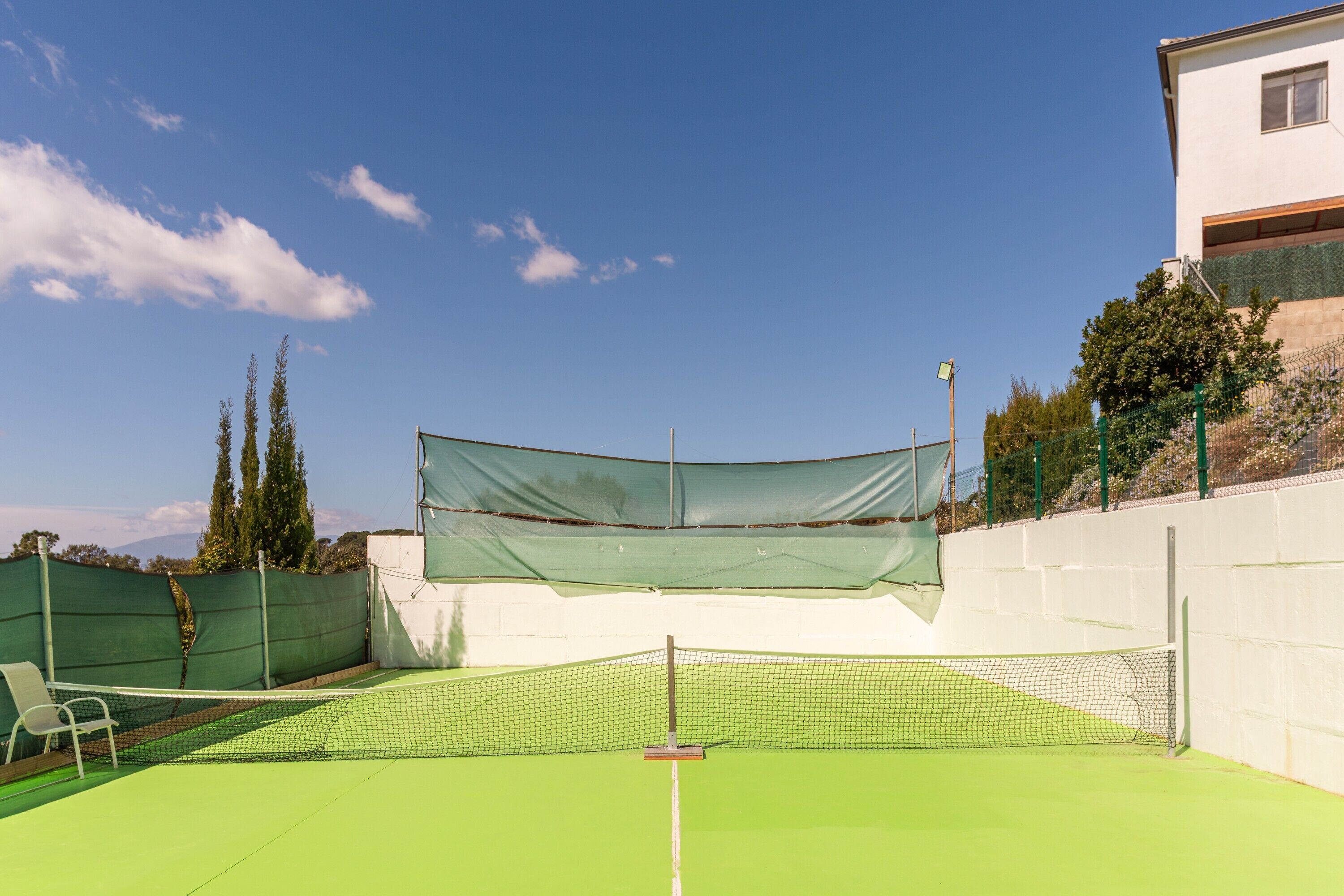 A tennis court with a net, a chair, and a building in the background.
