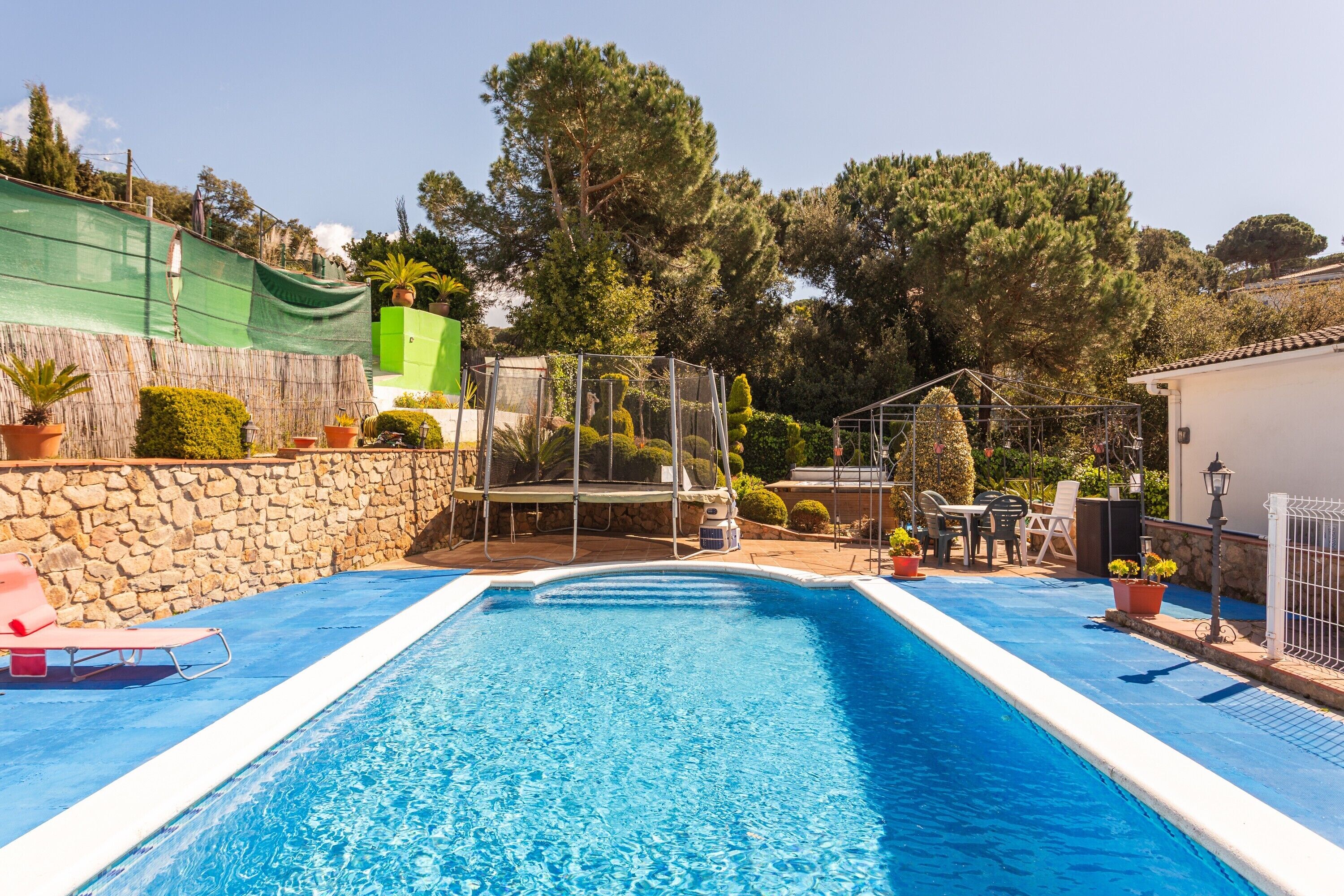 Ein Swimmingpool mit Steinmauer, einer Pergola und einem überdachten Bereich mit Stühlen und Tischen.