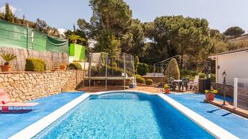 Ein Swimmingpool mit Steinmauer, einer Pergola und einem überdachten Bereich mit Stühlen und Tischen.