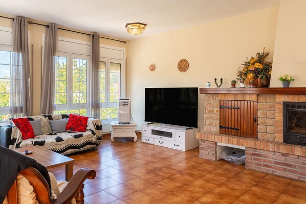 A living room with a TV, fireplace, sofa, and large windows. - Holiday Home 'Alicia y Rudi' with Wi-Fi (Vidreres)