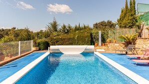 Une piscine rectangulaire bordée de blanc, entourée d’un mur de pierre et agrémentée de plantes en pot.