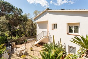A white building with a staircase, a patio with chairs and a table, and various plants. - Holiday Home 'Alicia y Rudi' with Wi-Fi (Vidreres)