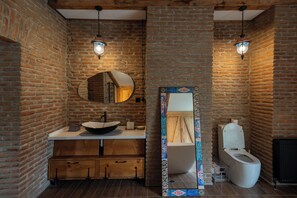 A bathroom with a brick wall, wooden cabinets, a sink, a mirror, and a toilet. - Hideout Across from Marjanishvili (Tbilisi)