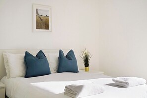 A neatly made bed with white and blue pillows, a small potted plant, and a folded towel on the bed. - New-Build 1-Bed Apartment in Luton (Luton)