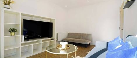 Una sala de estar moderna con un televisor de pantalla plana, un sofá, una mesa de centro de vidrio y un radiador.
