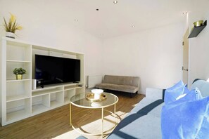 Ein modernes Wohnzimmer mit Flachbildfernseher, einer Couch, einem Glastisch und einer Heizung.