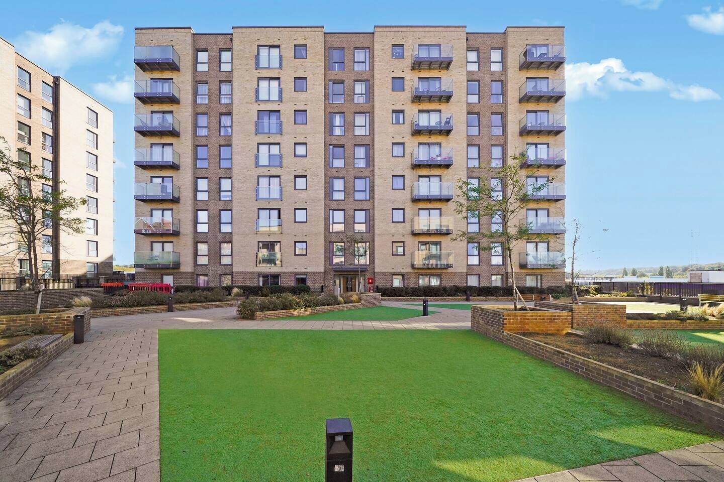 A multi-story residential building with balconies, a well-maintained lawn, and a brick pathway.