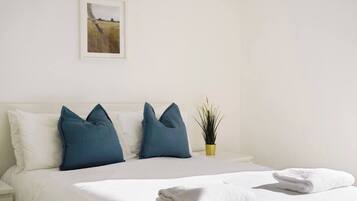 Una habitación de hotel con cama, almohadas, una planta pequeña y un cuadro en la pared.