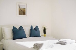 A hotel room with a bed, pillows, a small plant, and a framed picture on the wall. - New-Build 1-Bed Apartment in Luton (Luton)