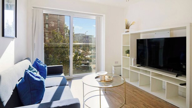 Una sala de estar moderna con un sofá, una mesa de centro de vidrio y un televisor sobre un mueble blanco.