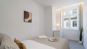 Een moderne slaapkamer met een bed, nachtkastje met lamp, raam met uitzicht en een potplant.