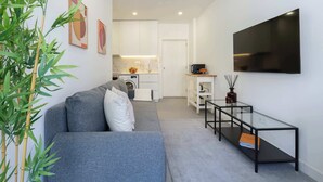 Een moderne woonkamer met een grijze bank, een glazen salontafel en een aan de muur bevestigde televisie.
