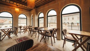 A restaurant with wooden tables and chairs, large arched windows, and a hanging light fixture. - Dream of Stones Cappadocia (Nevşehir)