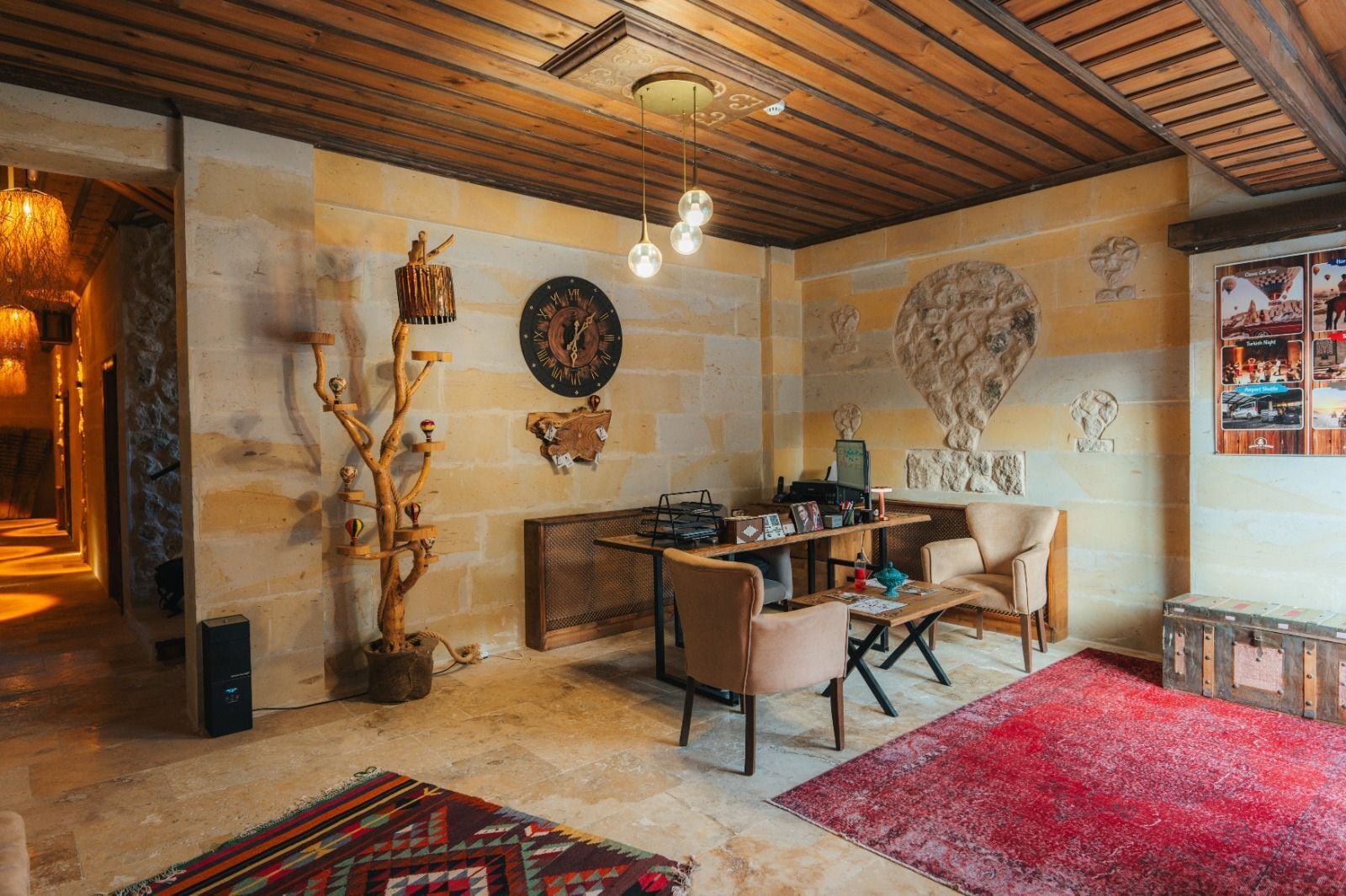 A cozy room with a wooden ceiling, a stone wall, a wooden coffee table, two chairs, a red rug, and a wall clock.