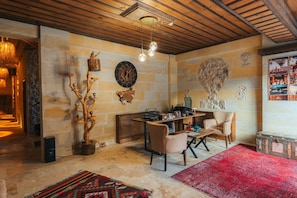 Une pièce chaleureuse avec un plafond en bois, un mur en pierre, une table basse en bois, deux chaises, un tapis rouge et une horloge murale.