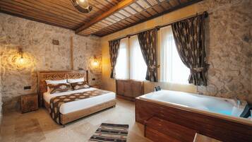 A bedroom with a large bed, a wooden headboard, a stone wall, a stone fireplace, and a large bathtub.