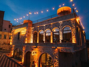 Un bâtiment en pierre doté de fenêtres en arc de cercle, une enseigne indiquant « Rêves de pierre » et des guirlandes lumineuses.