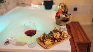 Una bañera de hidromasaje con un banco de madera, una bandeja de aperitivos y dos copas de vino tinto.