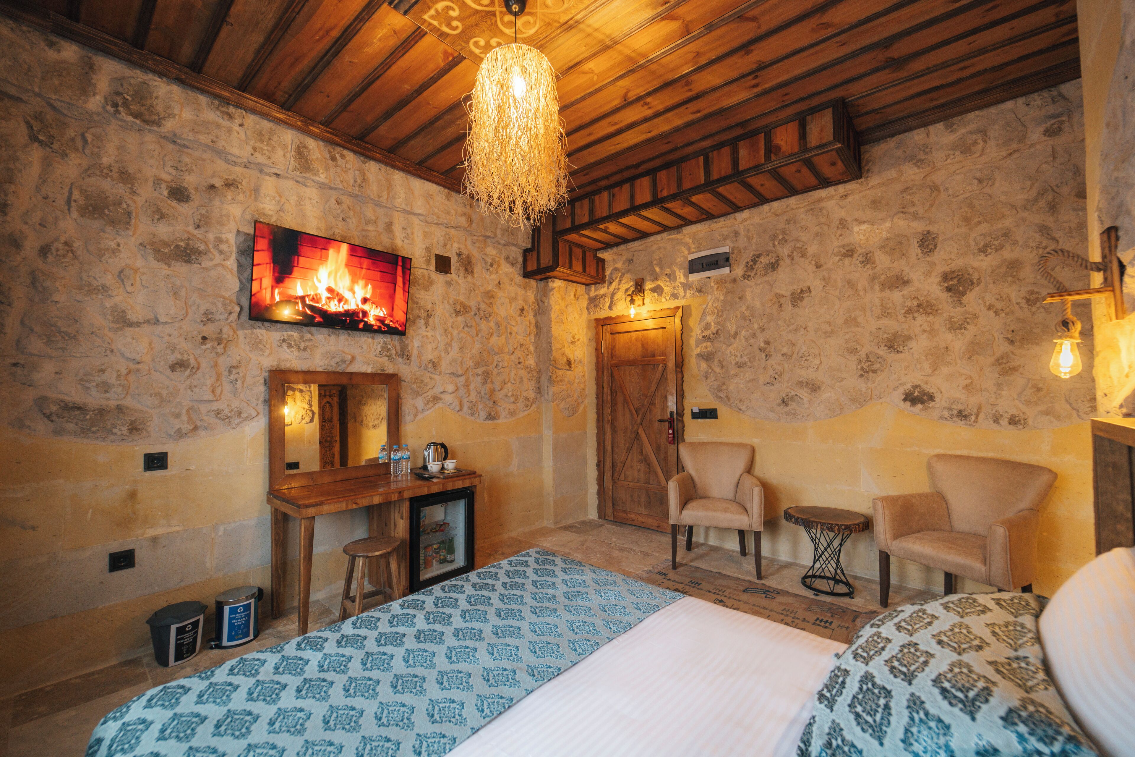 A cozy room with a bed, a desk, two chairs, a fireplace, and a stone wall.