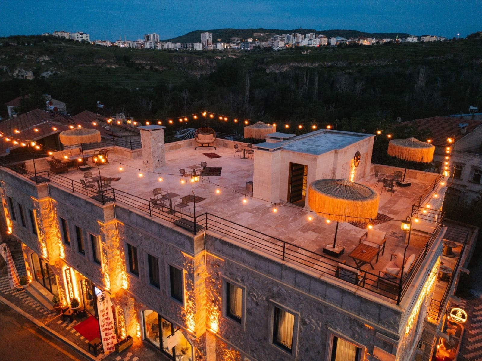 A rooftop terrace with outdoor seating, string lights, and a view of the cityscape.