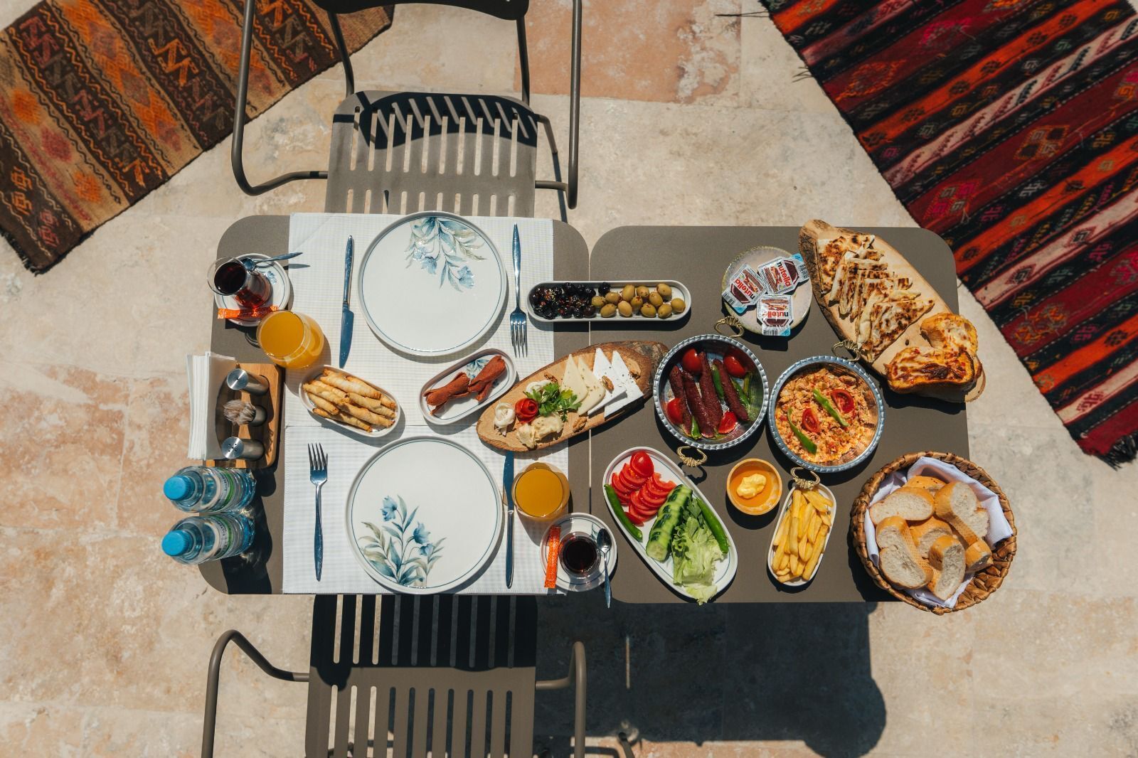 A table set outdoors with various dishes, drinks, and a chair.
