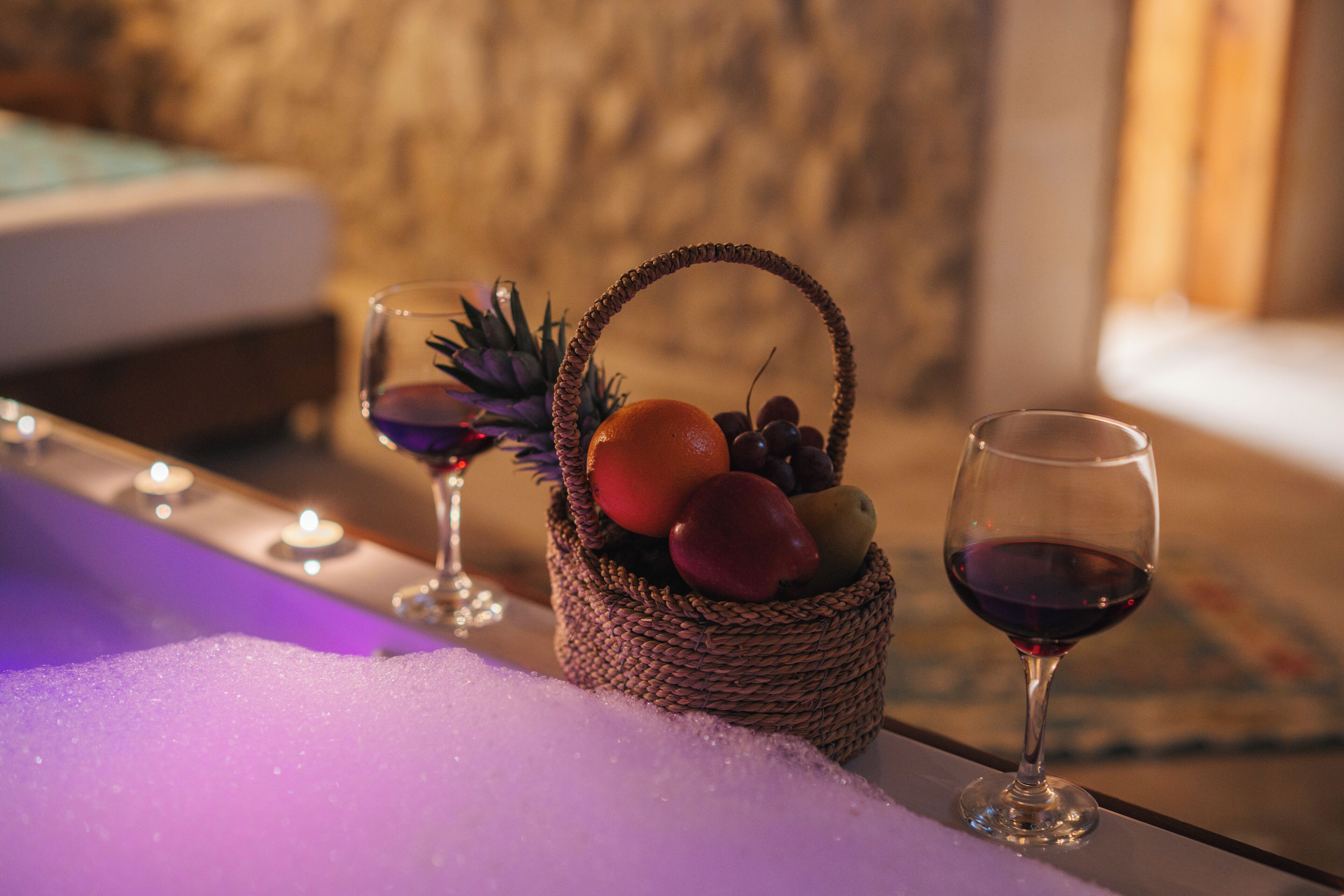 Una cesta de mimbre llena de frutas y una copa de vino tinto sobre una mesa con velas.