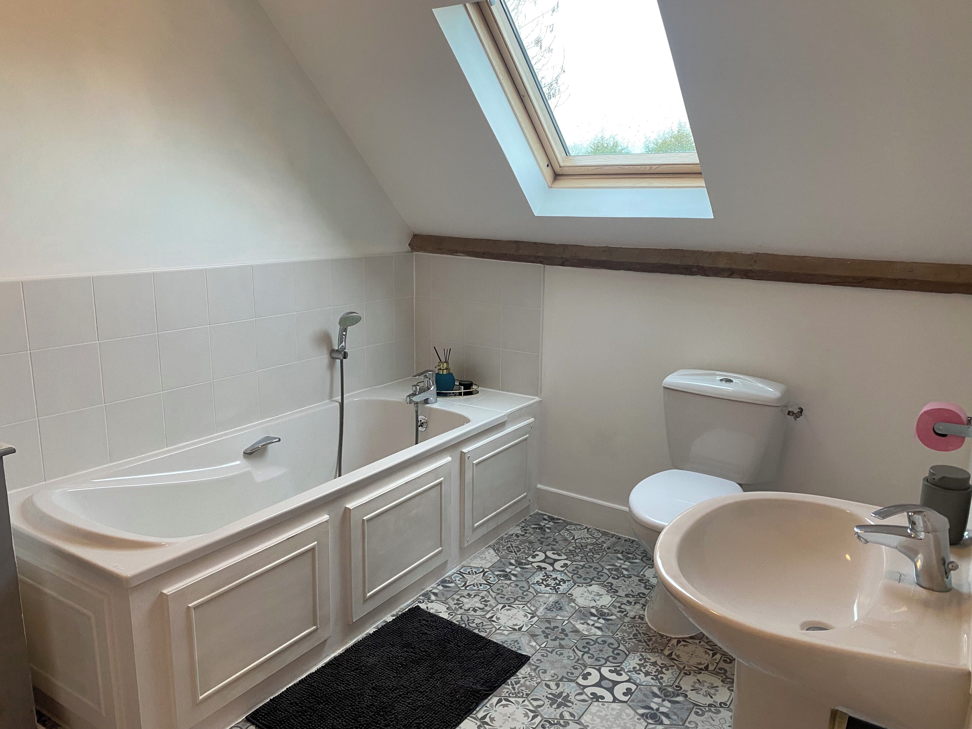 Ein Badezimmer mit Dachfenster, einer Badewanne, einer Toilette und einem Waschbecken.
