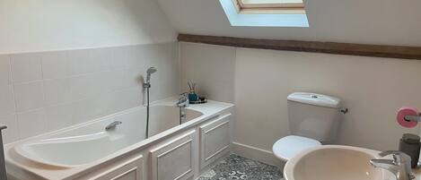 Ein Badezimmer mit Dachfenster, einer Badewanne, einer Toilette und einem Waschbecken.