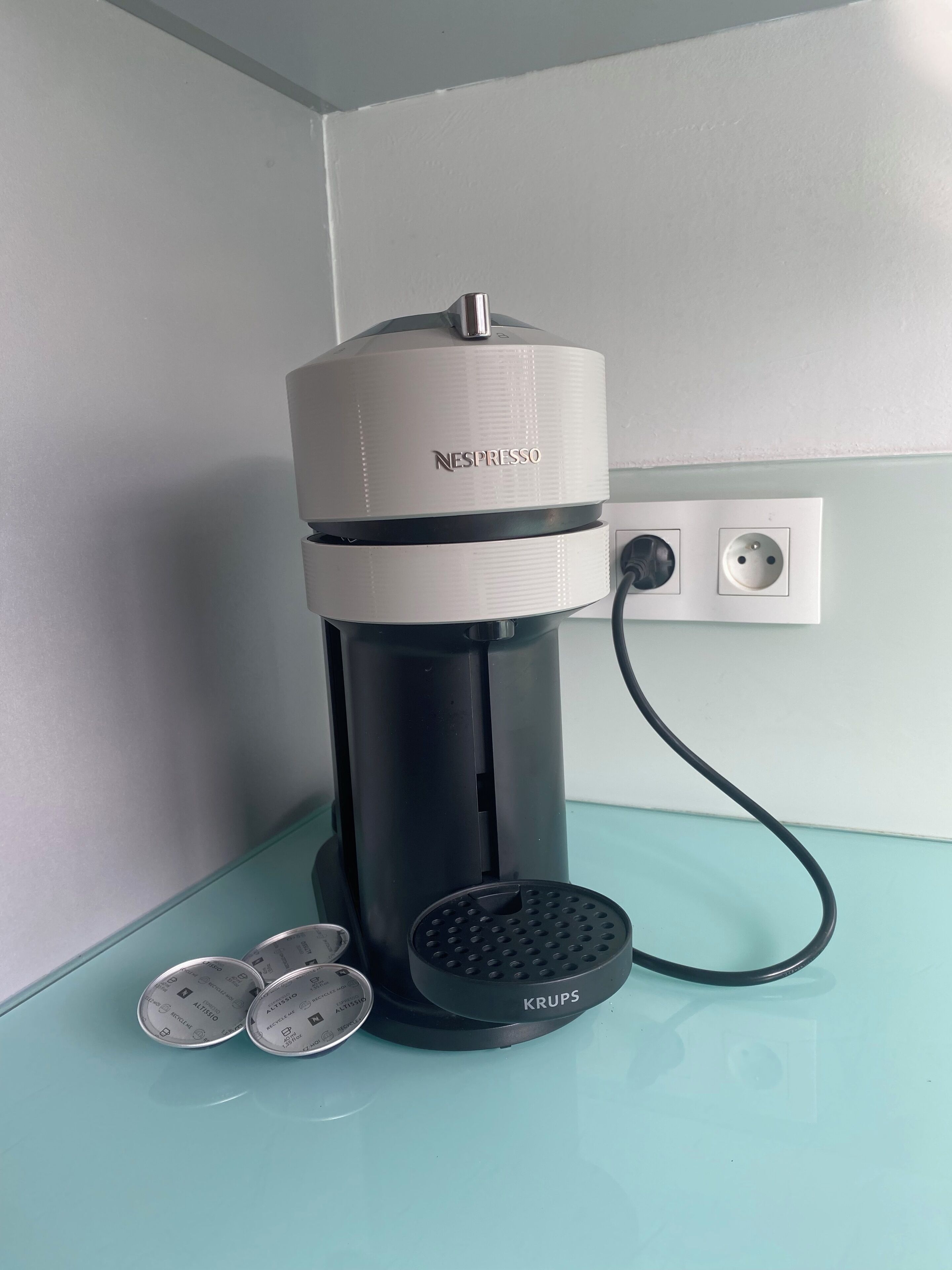 A Nespresso coffee machine with Krups coffee capsules on a teal countertop.