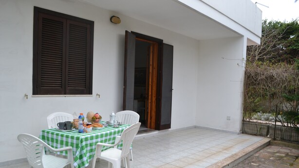 A patio with a checkered table and white chairs, a wooden door, and a white building facade. - Casa Amanda in Torre Dell'orso (Melendugno)
