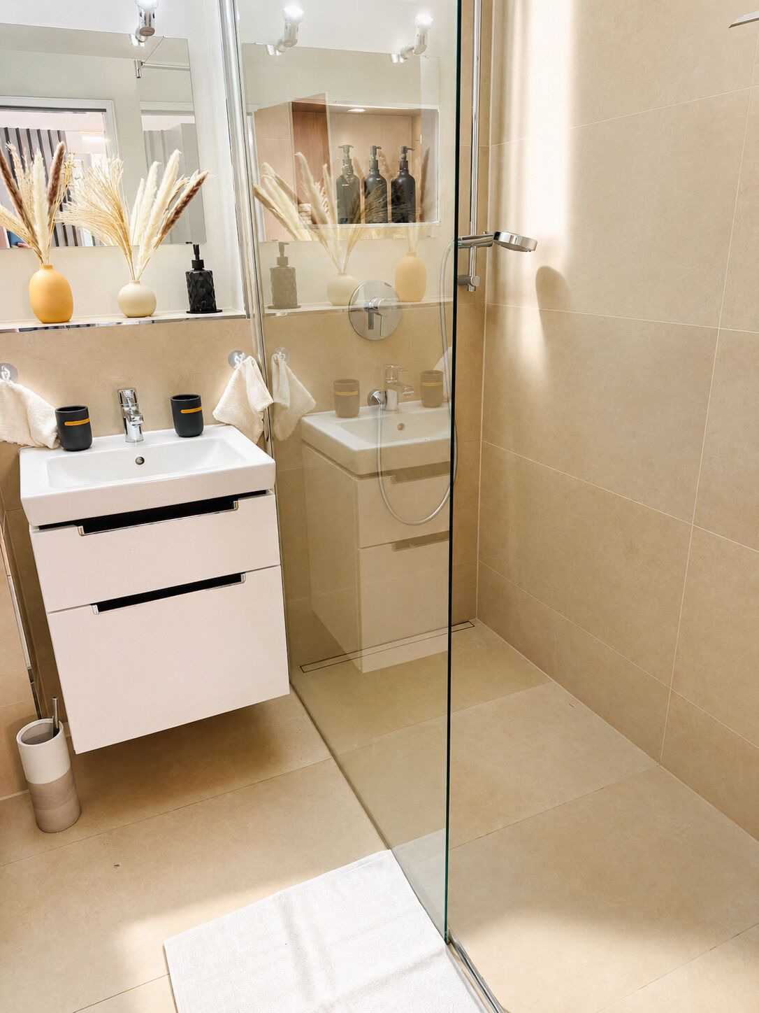 Een moderne badkamer met een douchecabine van glas, een witte wastafel met twee wasbakken en een spiegel boven de wastafel.